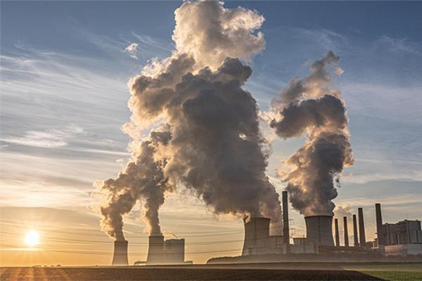 active smokestacks seen from accross an open field with sunset in background